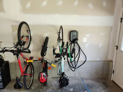 An electric vehicle charger mounted on a garage wall beside three bicycles on hooks
