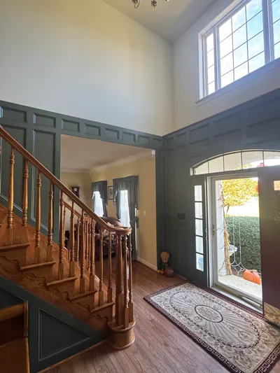 A two-story foyer with green raised paneling around the front door and along an oak staircase
