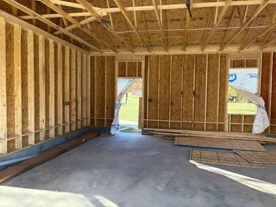 Inside the garage addition at framing: stud walls, roof trusses and a concrete floor, with cable already run across the ceiling