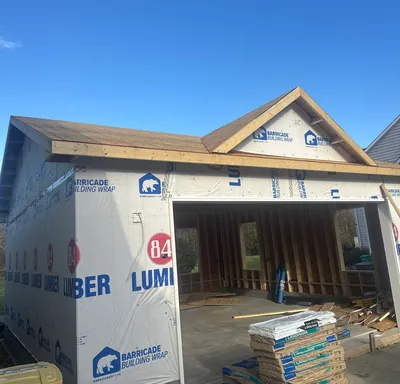 A garage addition framed, wrapped and roofed, with bundles of shingles stacked at the open bay
