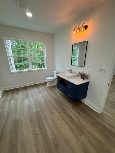 The loft bathroom: a floating navy vanity, a black framed mirror under a three-light fixture and a wide window