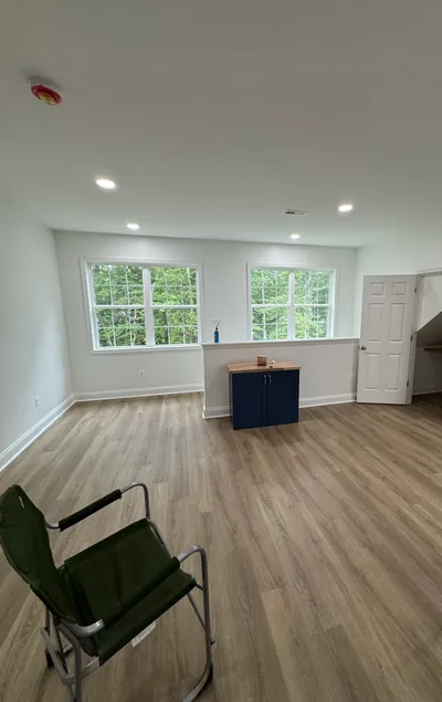 The carriage house loft as one open room: wood-look floor, recessed lights, two windows and a small navy cabinet island, a folding chair in the foreground