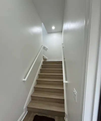 The stairwell to the loft, with wood-look treads, white handrails and a recessed light at the top