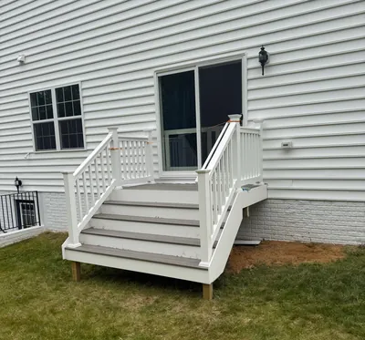 Composite steps and a landing with white railing at the sliding door of a white house